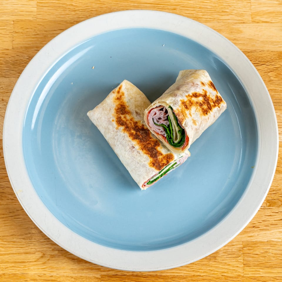 Two halves of a grilled ham and spinach wrap on a blue and white plate.