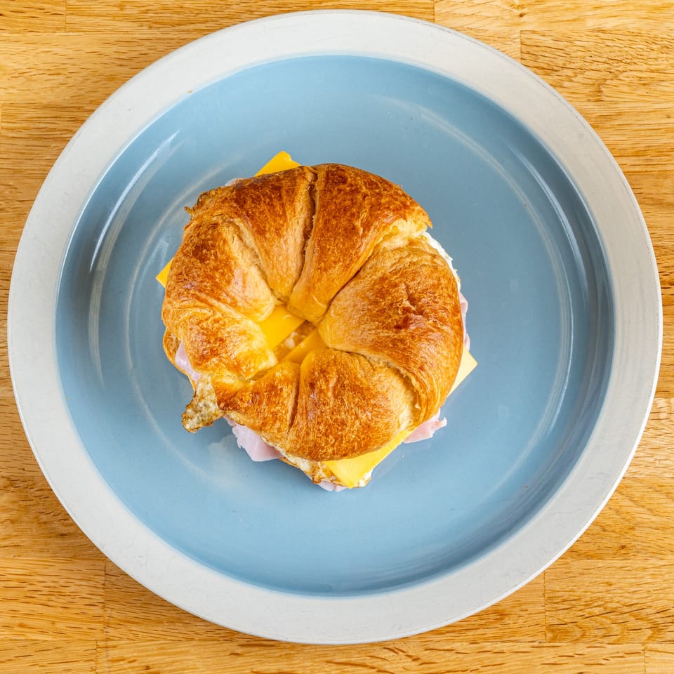 A croissant sandwich with ham, egg, and cheese on a blue plate, from Subs On The Run.