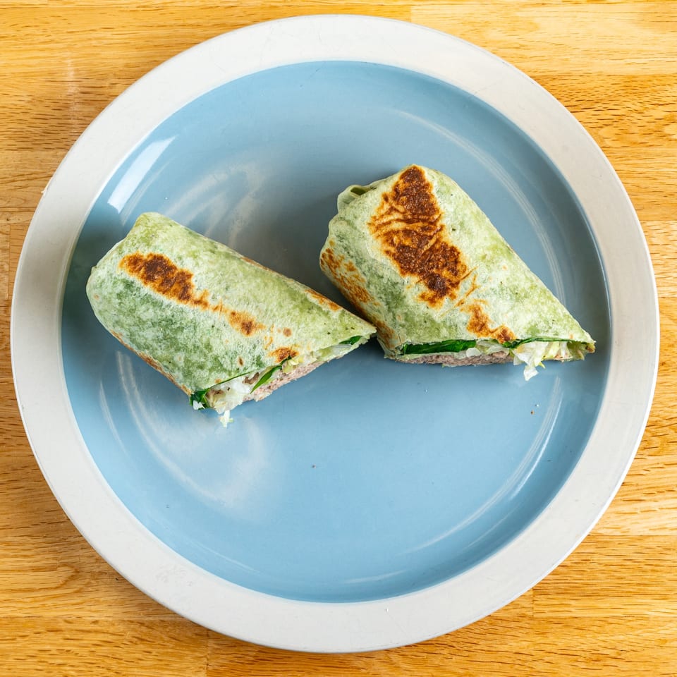 Two halves of a grilled green tortilla wrap, filled with meat and lettuce, on a blue plate.