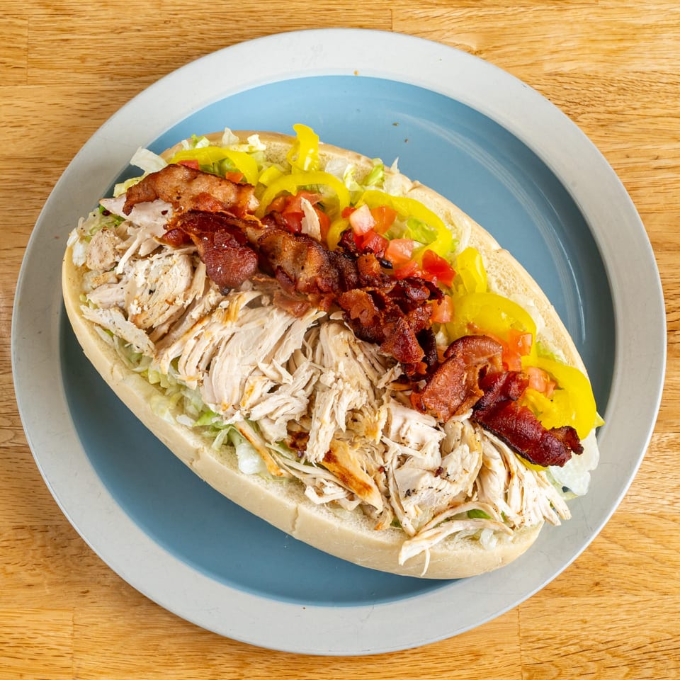 A chicken and bacon sub sandwich with lettuce, tomatoes, and yellow peppers on a blue plate.