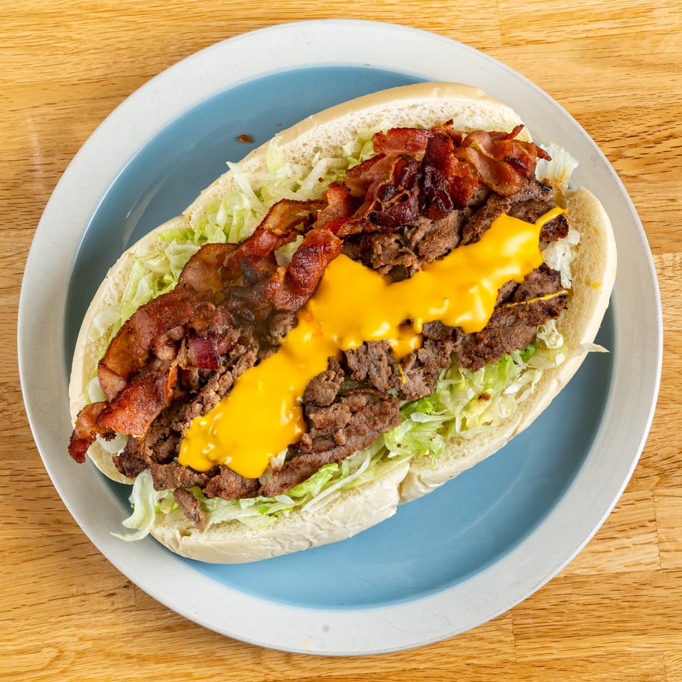 A bacon cheesesteak sub with shredded lettuce and melted cheese on a blue and white plate.