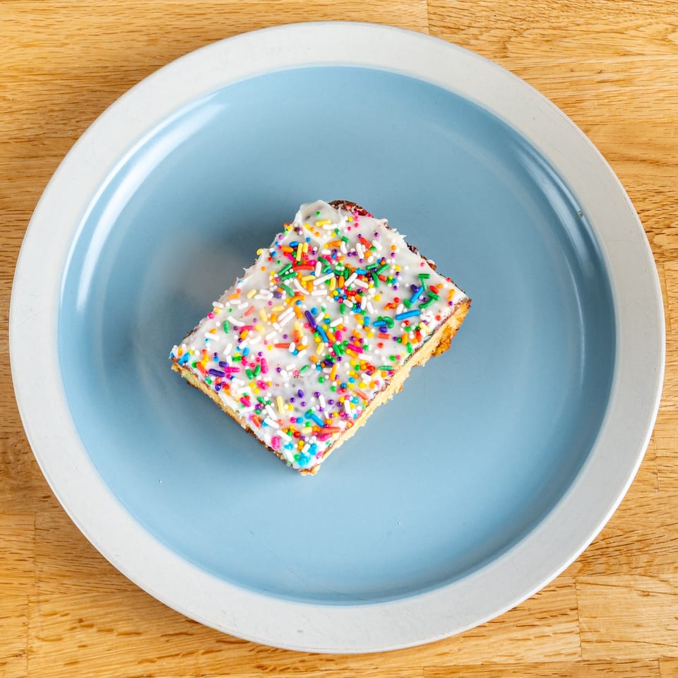 A rectangular dessert bar with white frosting and colorful sprinkles on a blue and white plate.