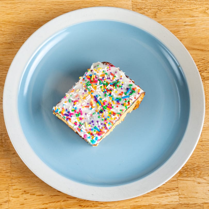 A rectangular dessert bar with white frosting and colorful sprinkles on a blue and white plate.