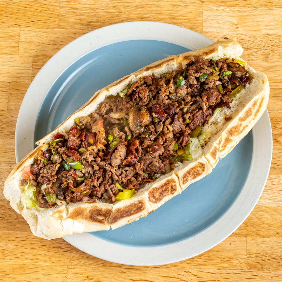 A large, open-faced cheesesteak sub with steak, peppers, and mushrooms on a blue plate.